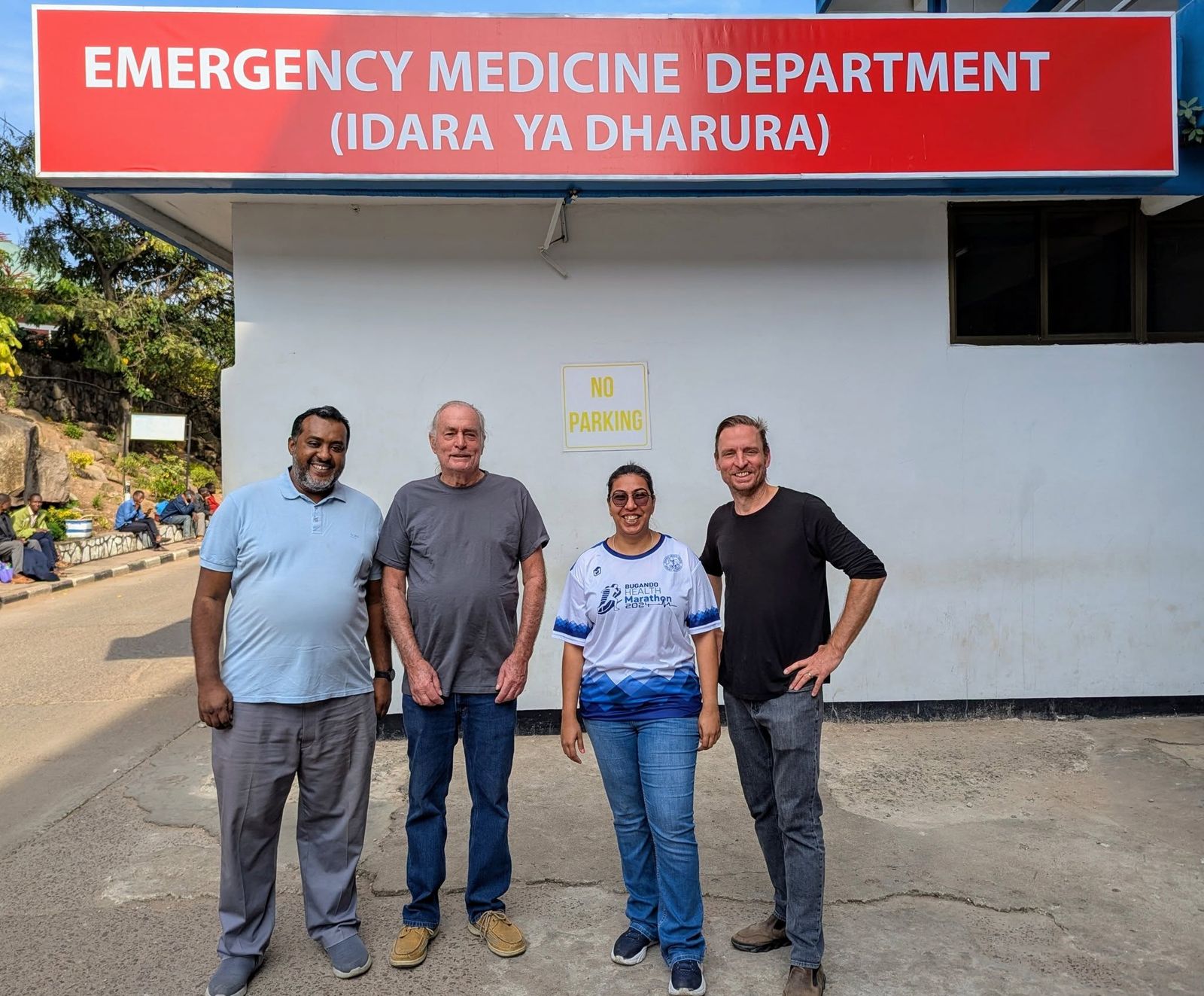 Four physicians standing outside the Bugando Medical Centre Emergency Medicine Department sign