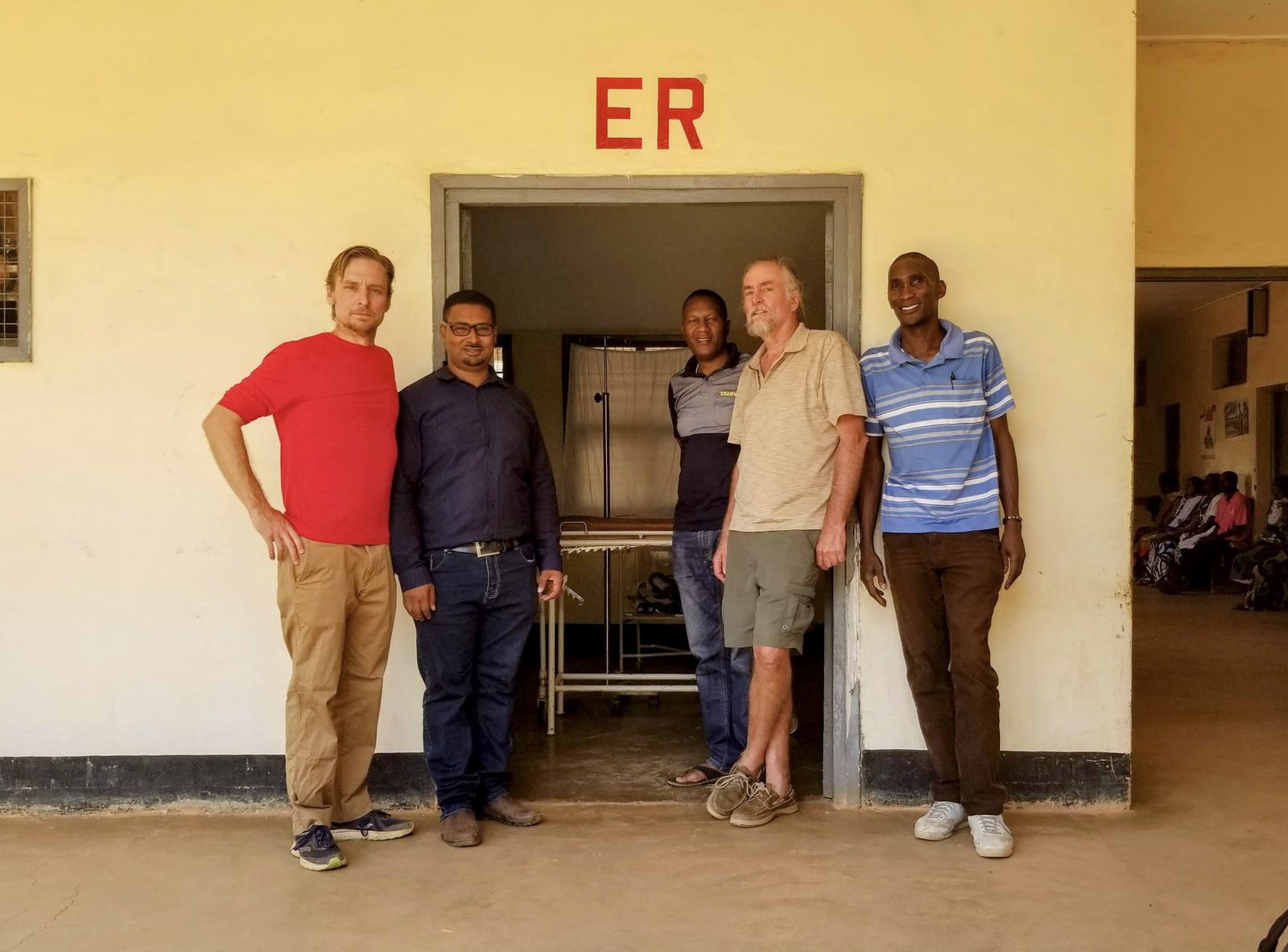 Five members of the emergency medicine team standing beneath the ER sign at Mpwapwa District Hospital