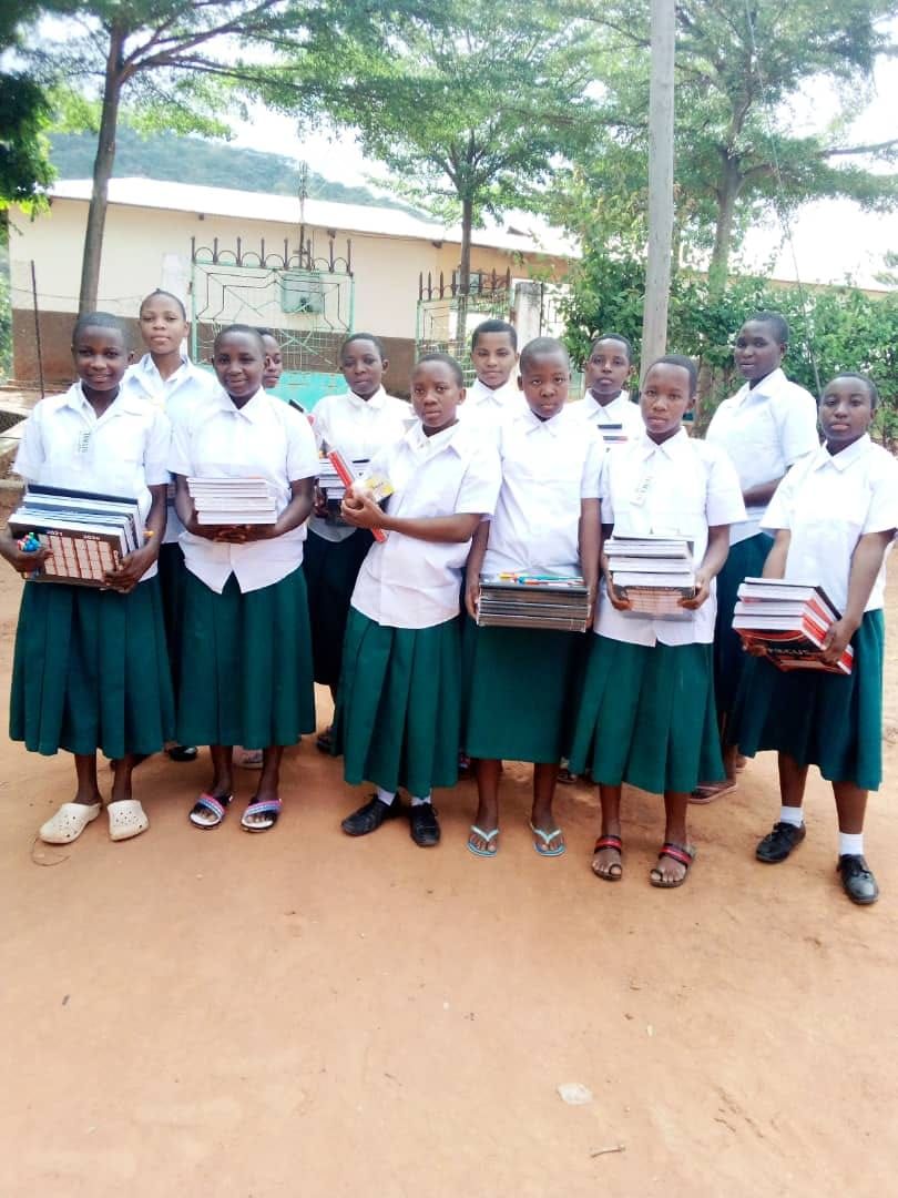 Girls in green and white uniforms holding boxes of school supplies